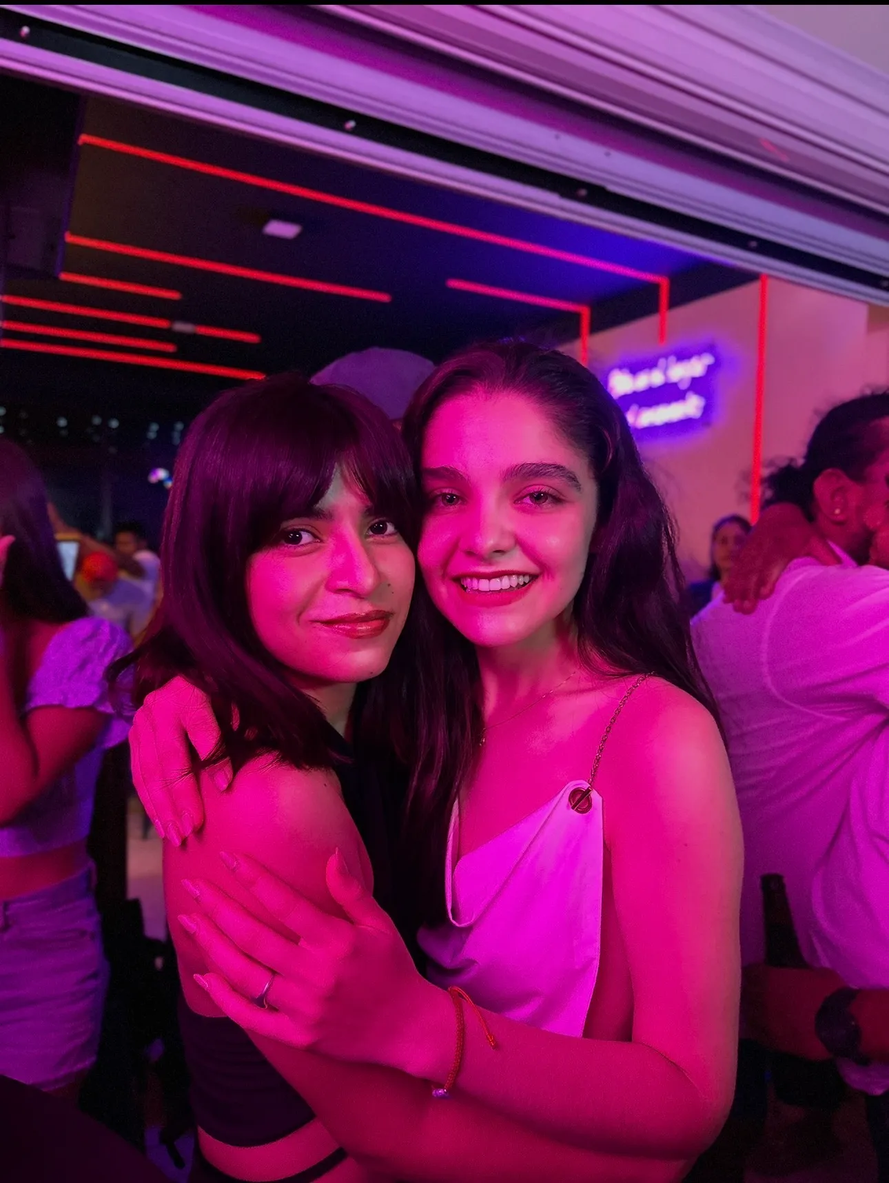 Amigas abrazadas bajo luces rosas